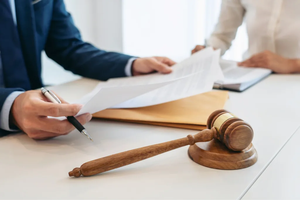 Charity Ignores Bequest Litigation and Pays the Price. Gavel on table with two people reviewing paperwork.